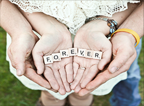 Two pairs of hands, holding wooden tiles spelling 'forever'