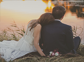 A couple sits before a lake at sunset